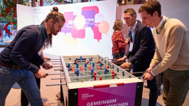 vier Menschen spielen Tischkicker vor der Logowand des BDEW Kongress 2024