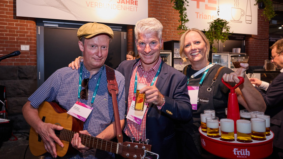 3 Menschen vor einer Bar mit Gitarre und Bier in den Händen