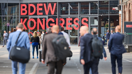 Menschen laufen auf eine Glasfassade mit der Aufschrift 'BDEW Kongress 2024' zu