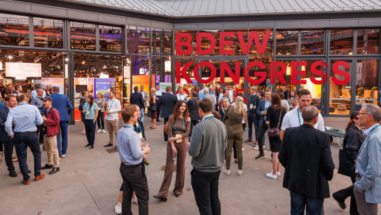 Menschen unterhalten sich vor einer Glasfassade mit der Aufschrift 'BDEW Kongress 2025'